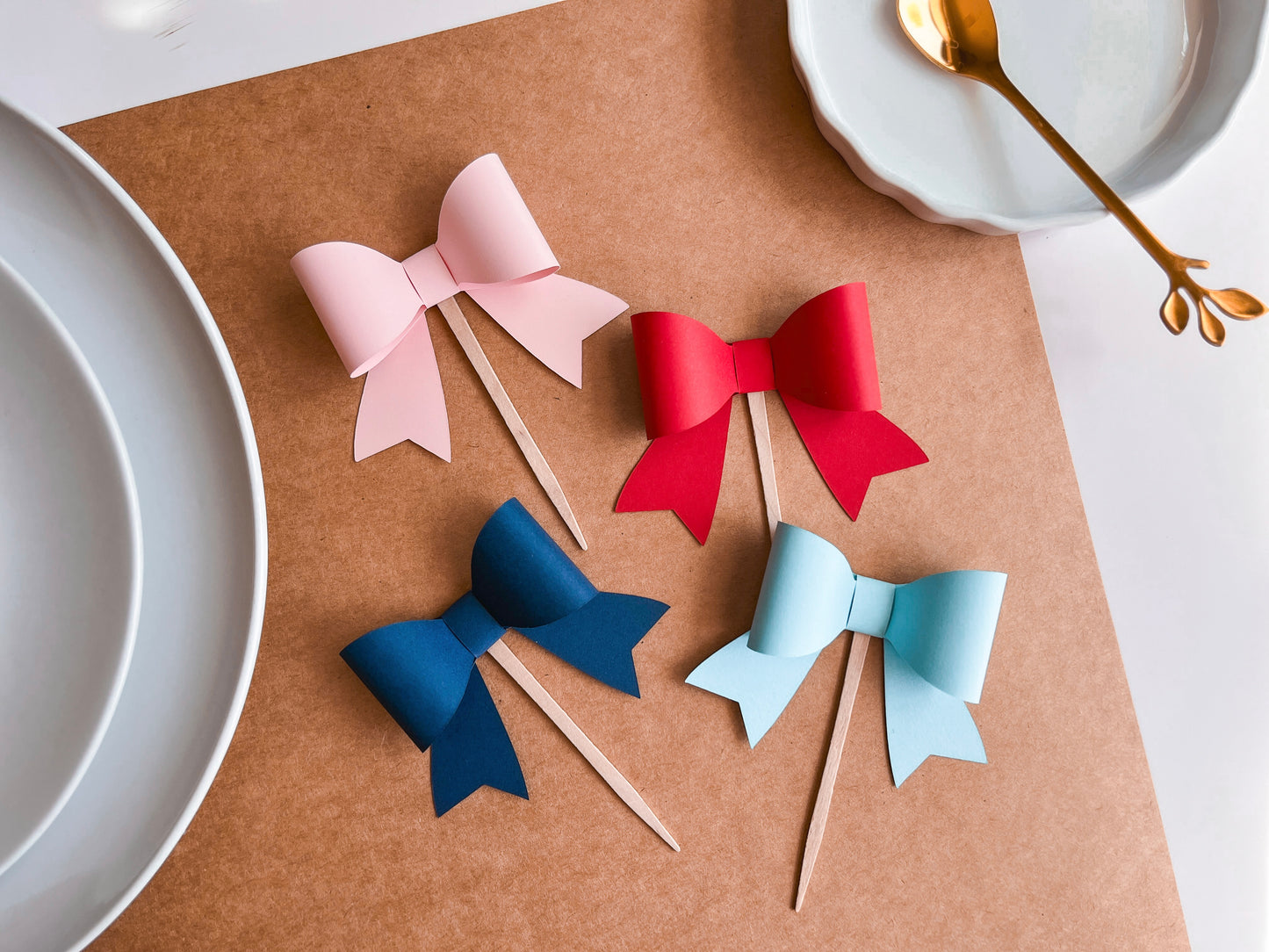 Set of 12 Bow Shape Cupcake Toppers affixed to food safe picks in pink, red, light blue, and navy blue.