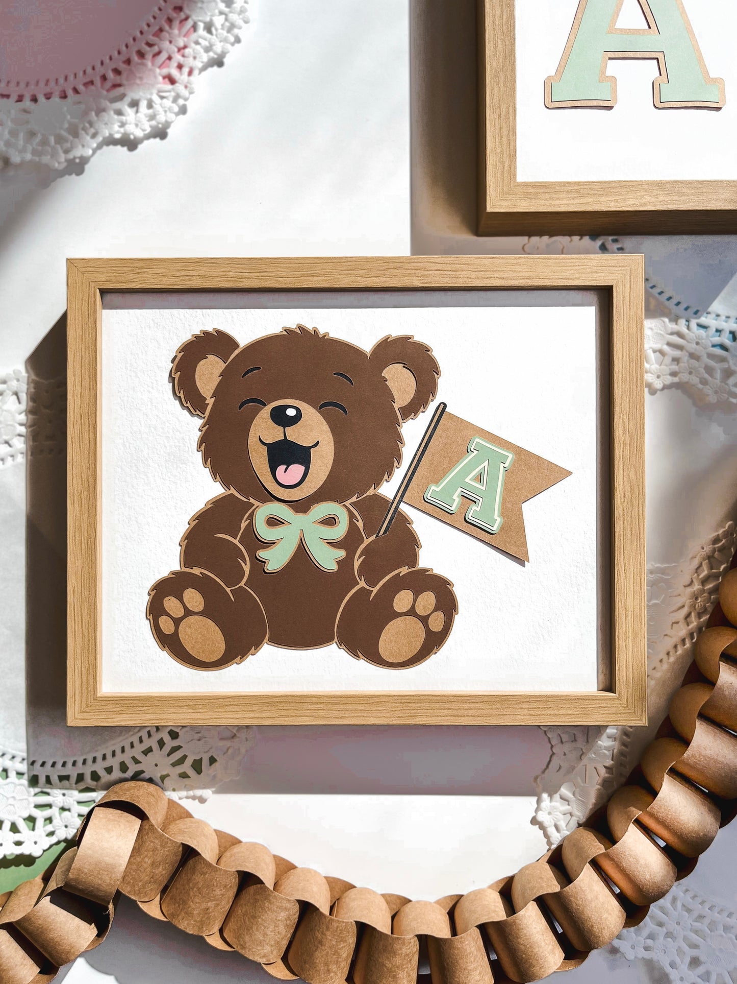 Framed picture of a teddy bear with a bow and banner on a decorative surface.