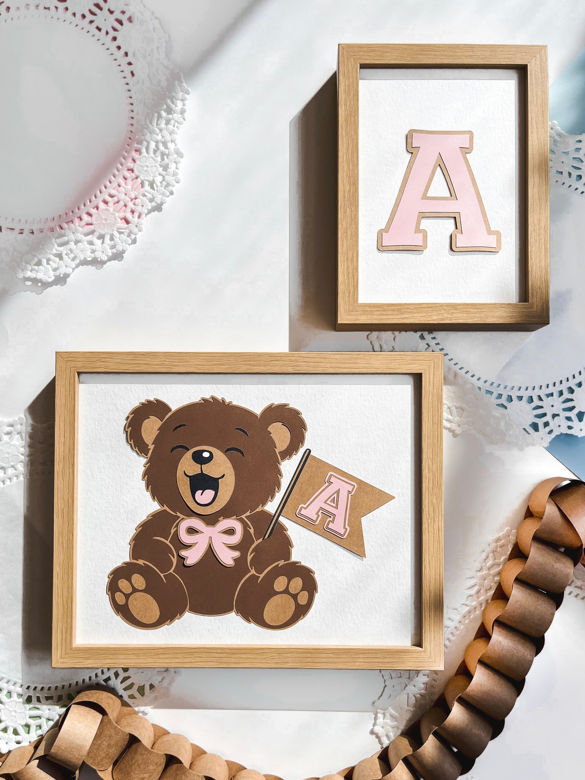 Framed picture of a teddy bear with a pink letter 'A' and a wooden frame on a white surface.