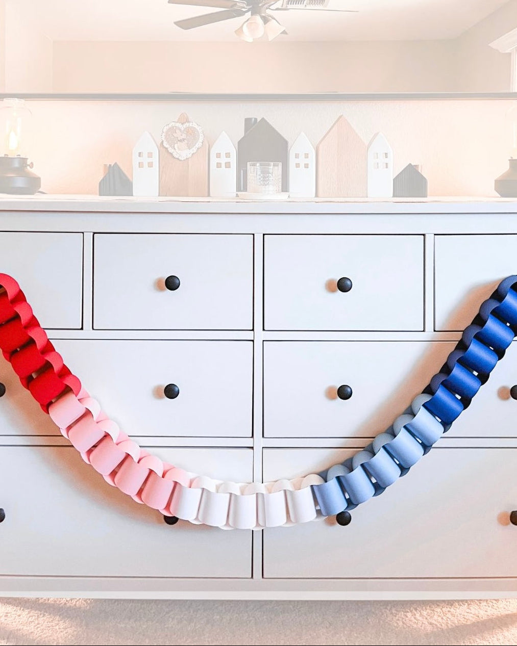 Colorful ribbon arch in front of a white dresser with decorative house-shaped boxes on a shelf.