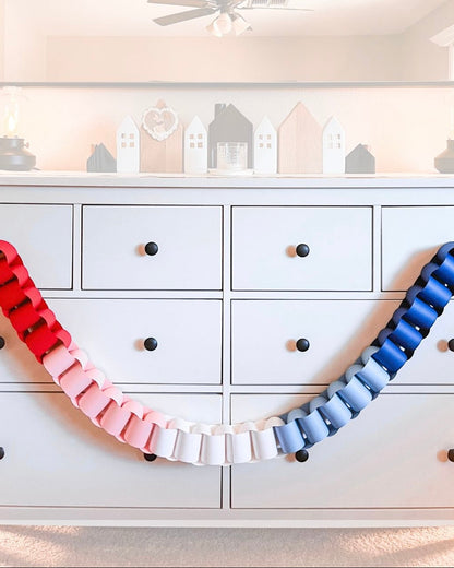 Colorful ribbon arch in front of a white dresser with decorative house-shaped boxes on a shelf.